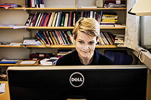 Elisabet Söderberg arbetar framför en datorskärm. I bakgrunden en bokhylla.
