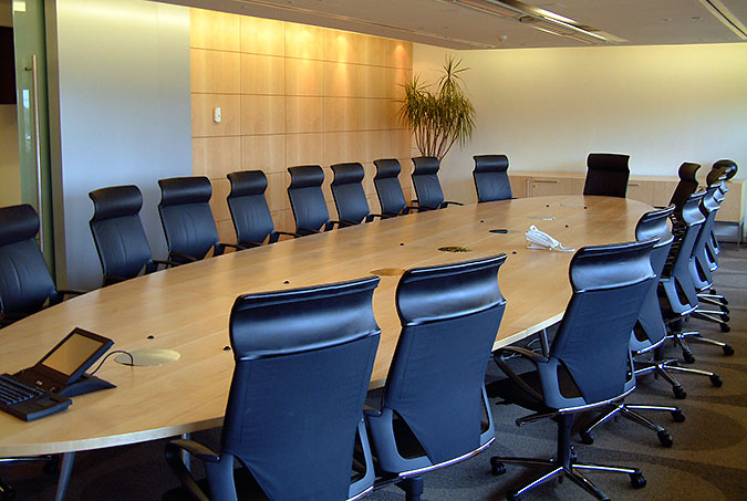 Ett sammanträdesrum med ett ovalt bord och blå stolar med höga ryggstöd.