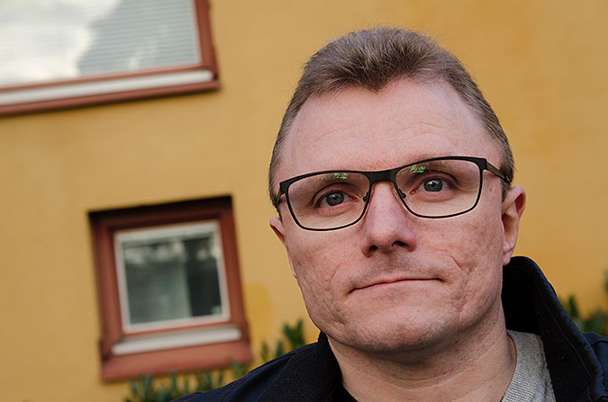 Porträtt av Lars-Göran Wadén framför en gul husvägg. 