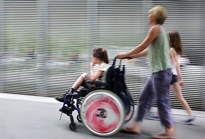 Flicka i rullstol blir körd av kvinna.