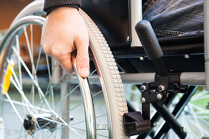 En bild på en hand som vilar på drivringen till ett rullstolshjul.