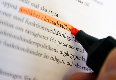En hand markerar med en rosa märkpenna texten jämlikhet i levnadsvillkor i en längre text på ett papper.