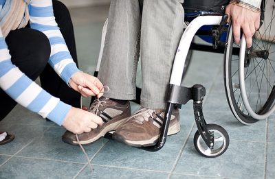 Armarna syns av en person som knyter skorna på en person som sitte i rullstol.