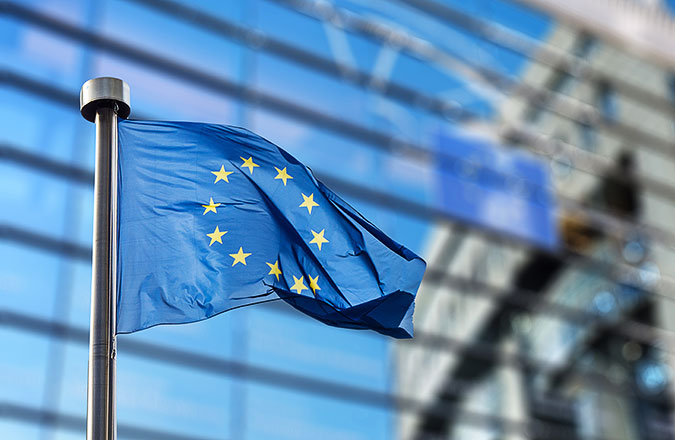En EU-flagga vajar framför en glasprydd fasad.