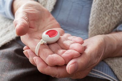 En hand hos en äldre person håller en larmknapp till trygghetslarmet.