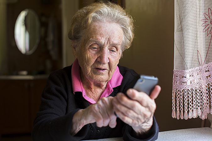 En äldre kvinna sitter vid ett bord och trycker på en smart mobil