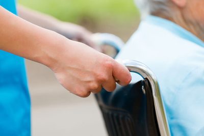 En äldre person blir körd i rullstol av en yngre.