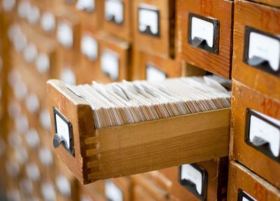En utdragen arkivskåpslåda i trä med massor av arkivkort i. Lådan är en del av ett större skåp med många likadana lådor.