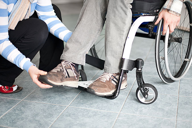 En person som sitter i rullstol får hjälp att få foten på plats på fotplattan.