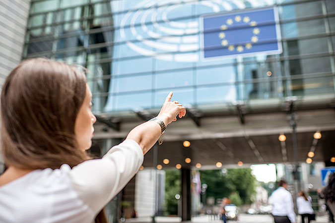 En kvinna pekar mot en fasad där det hänger en EU-flagga.