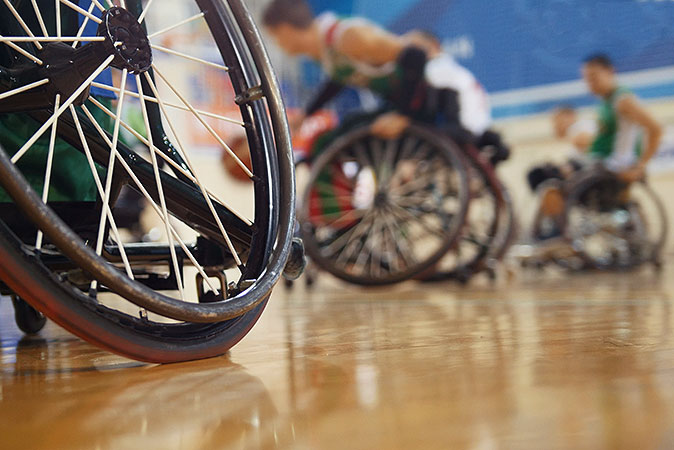 Bild i grodperspektiv på personer i rullstolar som utövar sport i en idrottshall.