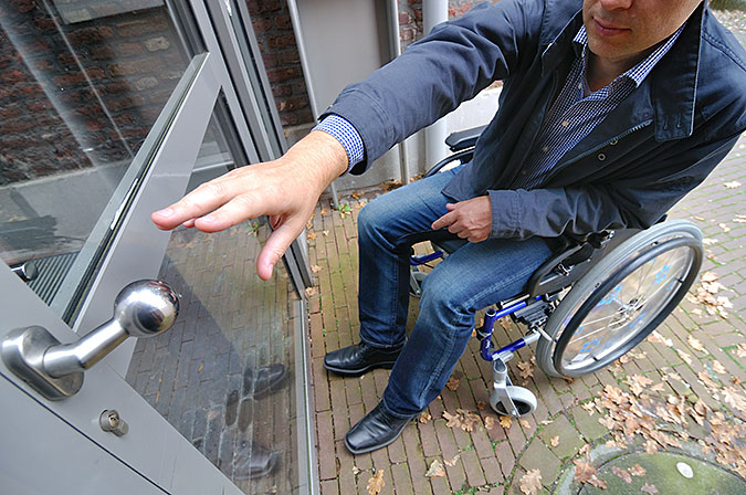 Man sittande i rullstol försöker att öppna en ytterdörr.