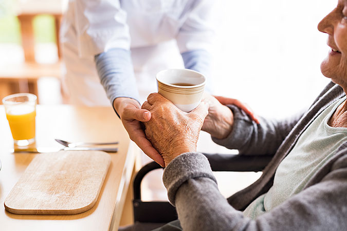En person hjälper en äldre person att hålla en mugg med kaffe
