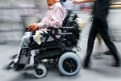 En suddig bild på en man i elrullstol som ackompanjeras av en annan person.