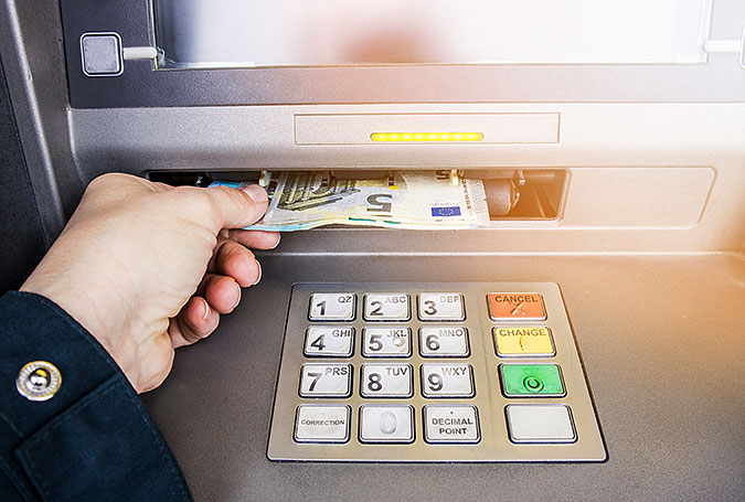 En hand tar ut euro-sedalr ur en bankomat. På bilden syns även knappsatsen.