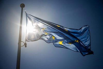 En EU-flagga fladdrar i vinden med solen i bakgrunden.