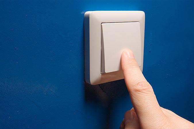 Ett finger trycker pop en strömbrytare på en blå vägg.