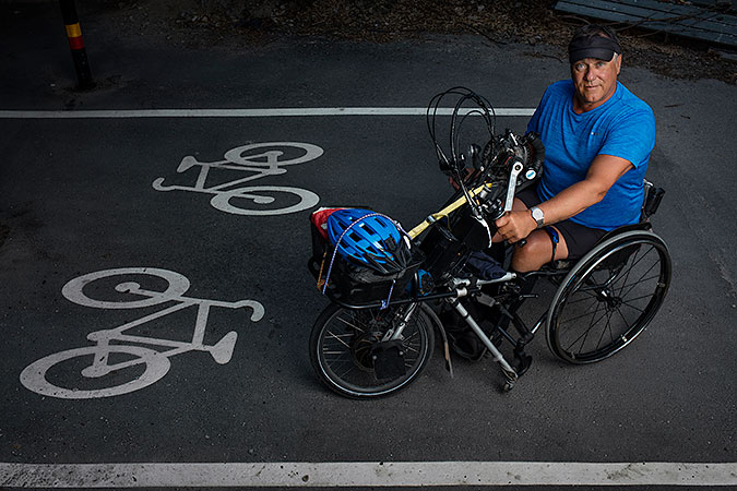 Björn Billung sitter i sin rullstol med en armcykel kopplad till. Han befinner sig på en dubbelriktad cykelbana. Två cykel-symboler är målade på asfalten.