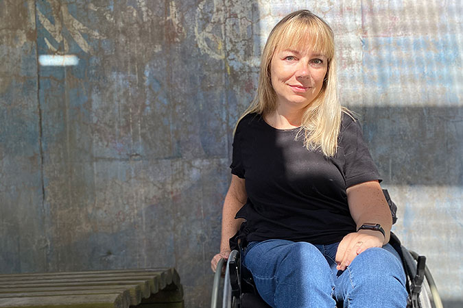 porträtt av Pia Hammagren. Hon sitter i en rullstol framför en spräcklig betongvägg.