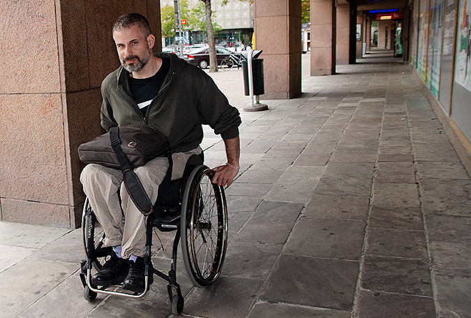 Rasmus Isaksson rullar i sin rullstol i en arkad utanför en byggnad.