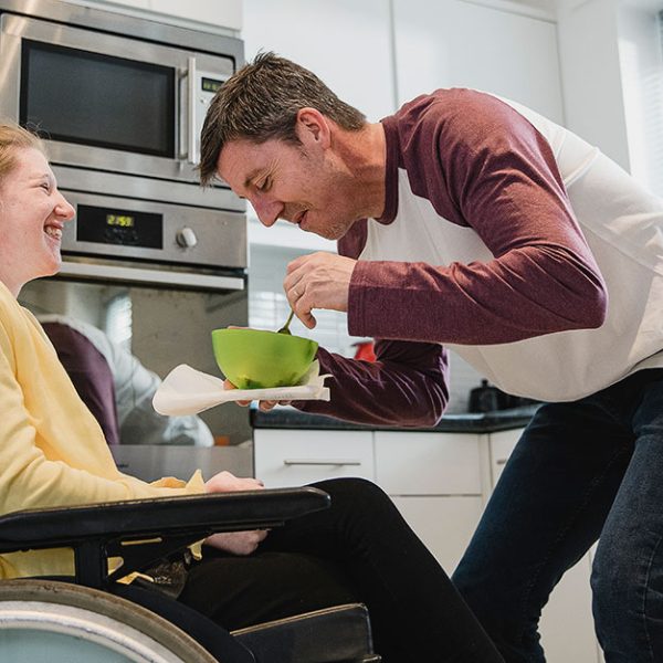 En man hjälper en kvinna i rullstol med maten.