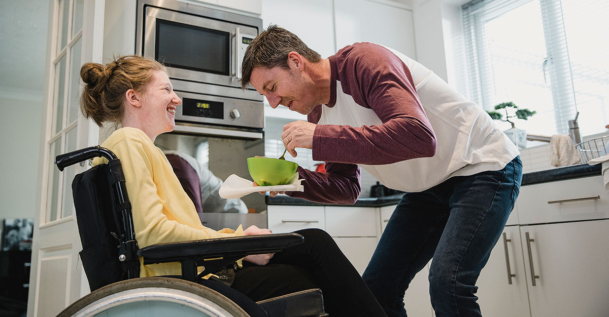 En man hjälper en kvinna i rullstol med maten.