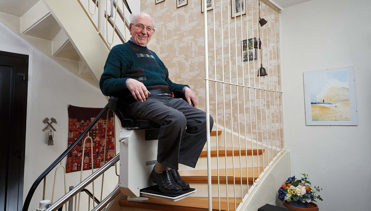 Äldre man sitter i en trapphiss på väg upp eller ned för en trappa.