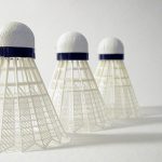 Tre badmintonbollar står på en ljus yta med ljuset fallande in från vänster.
