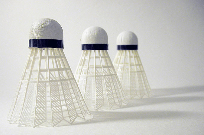 Tre badmintonbollar står på en ljus yta med ljuset fallande in från vänster.