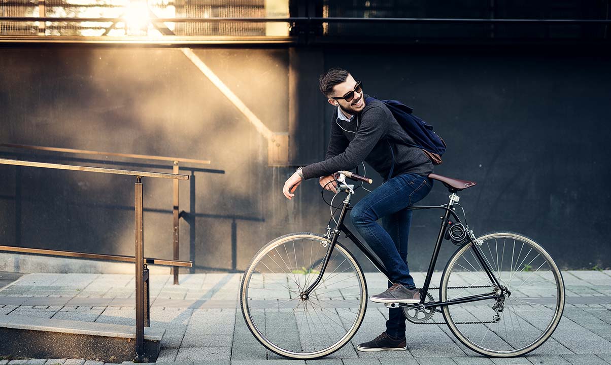 Man av yngre modell står gränsle över sin cykel framför an byggnad som ser hyggligt ny ut.