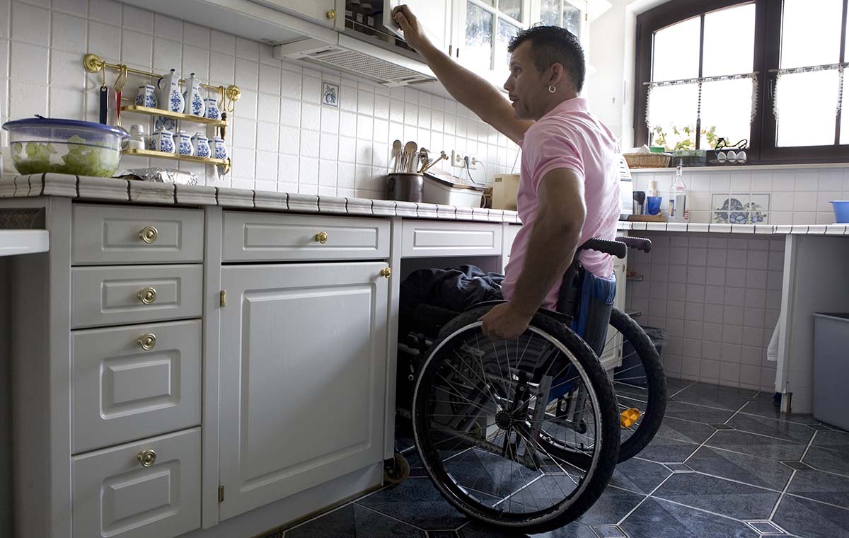 En man i rullstol sträcker sig för att öppna luckan till ett köksskåp.