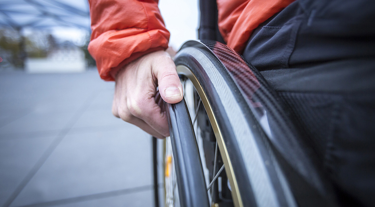 En närbild på en hand som vilar på drivringen till ett rullstolshjul