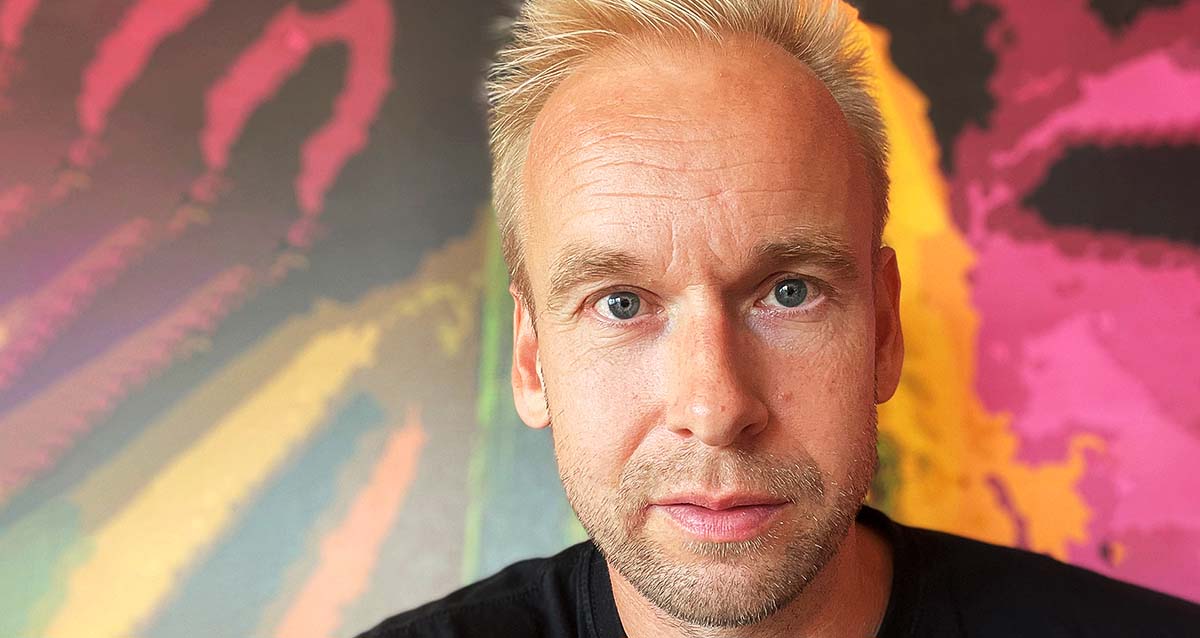 Porträtt av Stefan Johansson mot en mångkollorerad bakgrund.