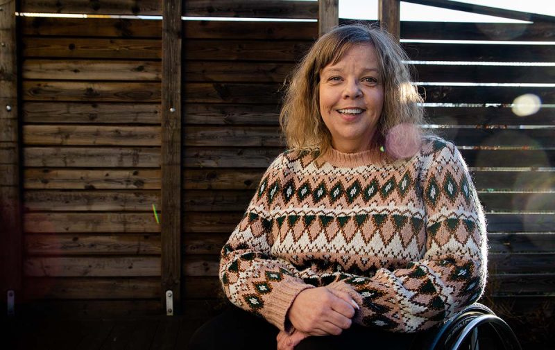 En leende Åsa Strahlemo iförd en stickad tröja. Hon sitter utomhus med ett plank i bakgrunden.