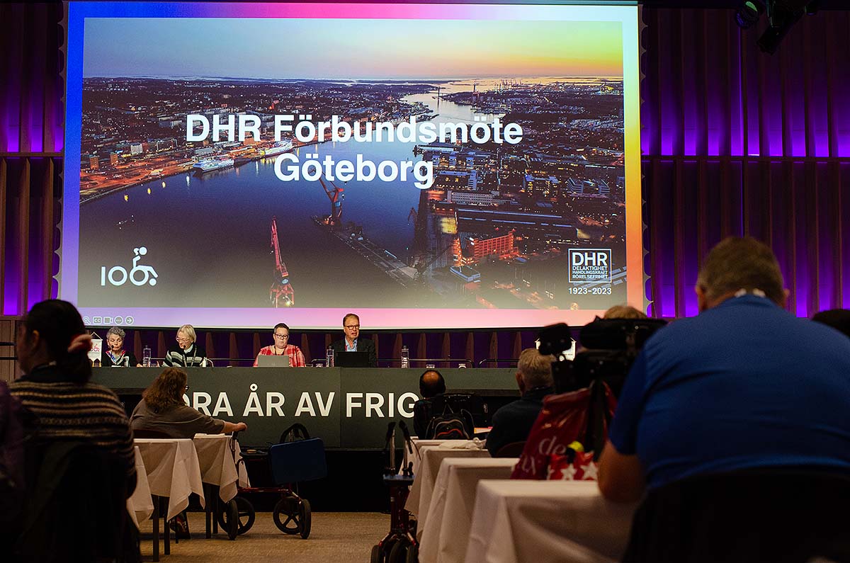 En bild från möteslokalen Göteborg. I förgrunden ses några ombud som är vända mot presidiet. I bakgrunden sen stor skärm med texten DHR Förbundsmöte Göteborg.