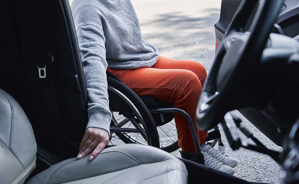 En person med röda byxor isitter i en rullstol utanför en bil, redo att hoppa in i förarsätet.