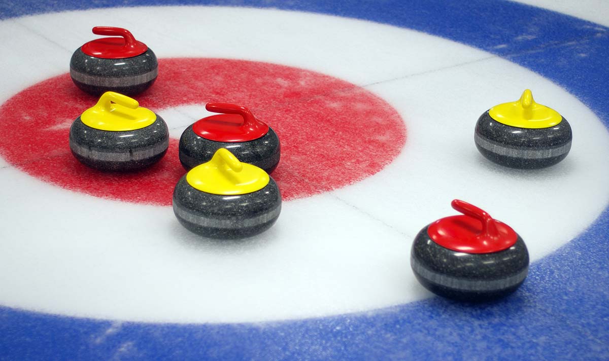 Tre röda och tre gula curlingstenar trängs i målområdet på en curlingbana.
