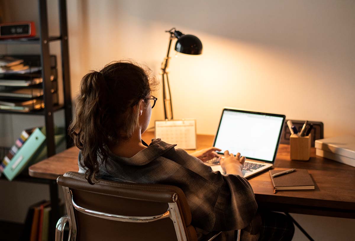 En kvinna sitter vid ett skrivbord och tittar på sin dator. Det ser ut som en studentbostad.