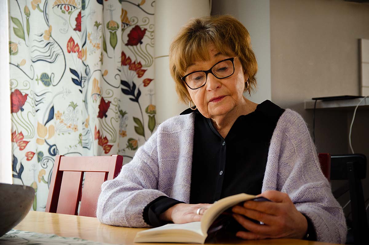 Margareta Persson sitter vid ett bord och läser i en bok.