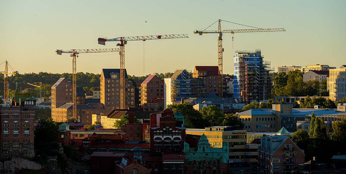 Flerbostadshus och byggkranar bryter av mot en ljuskvällshimmel.