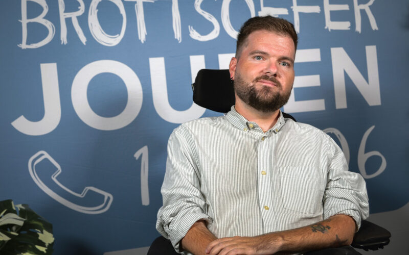 Porträtt av Tobias Holmberg där han sitter framför en vägg där det står Brottsofferjouren.