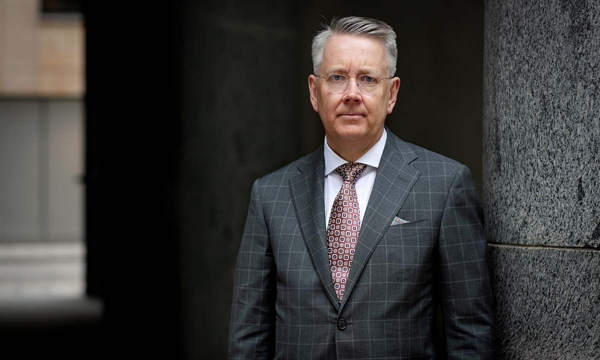 Porträtt av en man i kavaj och slips som står lutad mot en stenpelare.