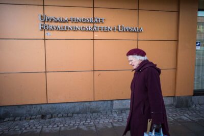 En äldre kvinna passerar framför en vägg med skyltar för Uppsala Tingsrätt och Förvaltningsdomstolen i Uppsala.
