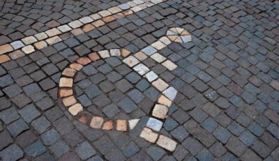 En rullstolssymbol infogad med vita stenar i en en markbeläggning av smågatsten.