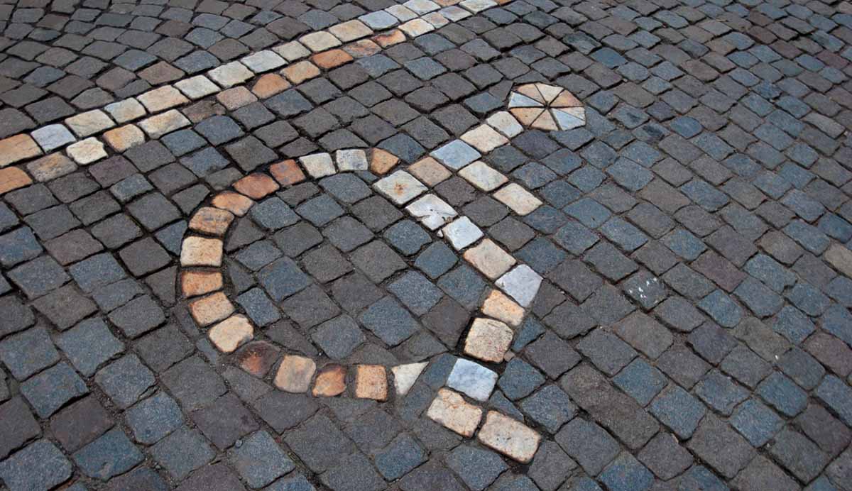 En rullstolssymbol infogad med vita stenar i en en markbeläggning av smågatsten.