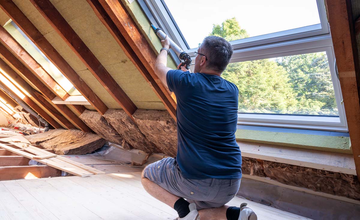 En man tätar ett till synes nyinstallerat takfönster på en vind som håller på att byggas om.